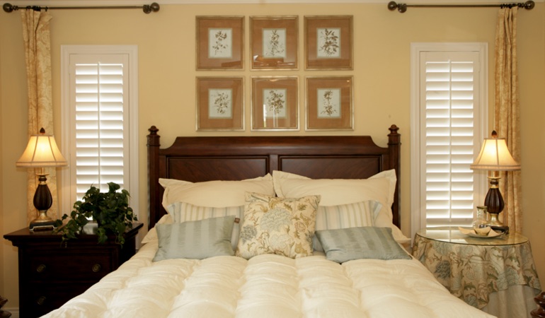 Beige bedroom with white plantation shutters covering windows in Gainesville 